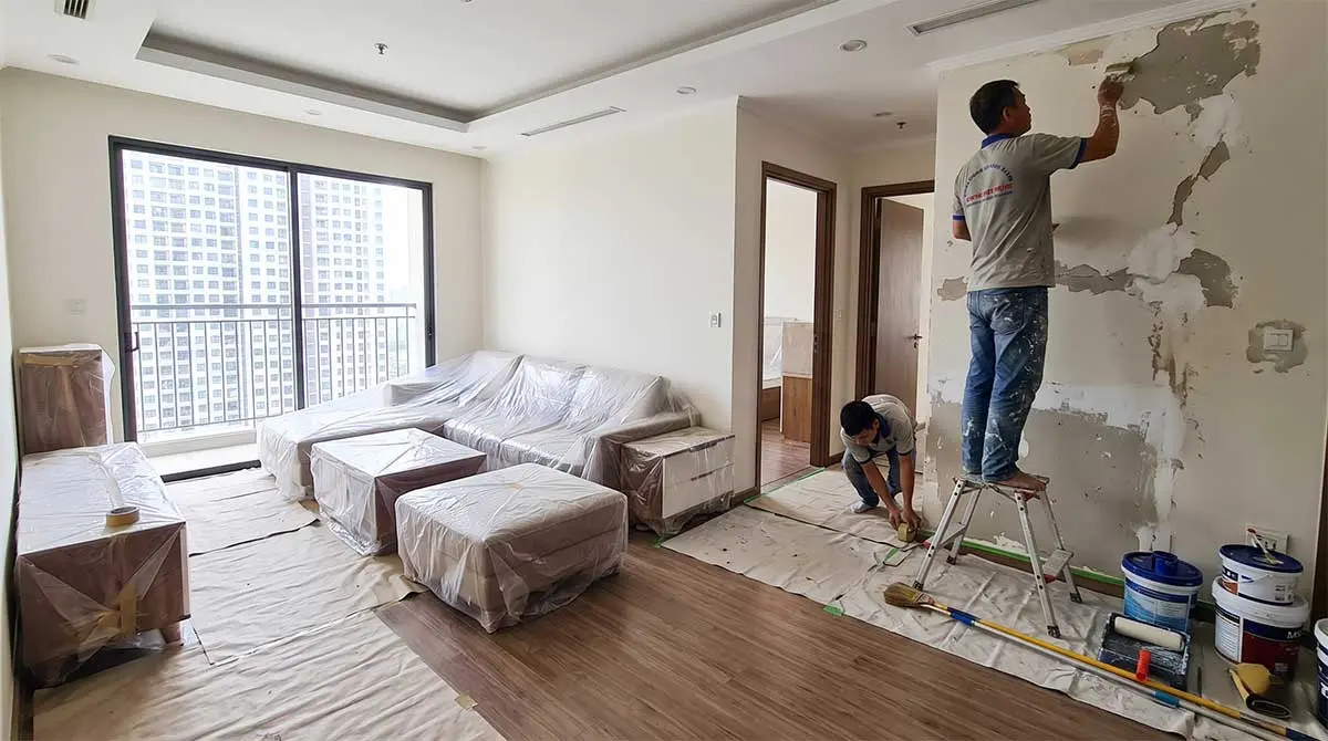 Thợ sơn che chắn đồ đạc bằng nilon và bả matit xử lý nền tường trước khi sơn nhà chung cư. Thợ sơn che chắn đồ đạc bằng nilon và bả matit xử lý nền tường trước khi sơn nhà chung cư.